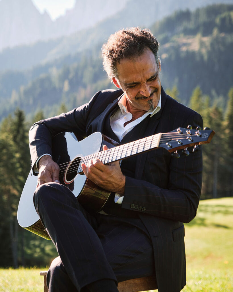 Guitarist playing a Thom Orgler Latemar acoustic (PU high-gloss Smokegrain) outdoors in the Dolomites, eyes closed, enjoying the performance.