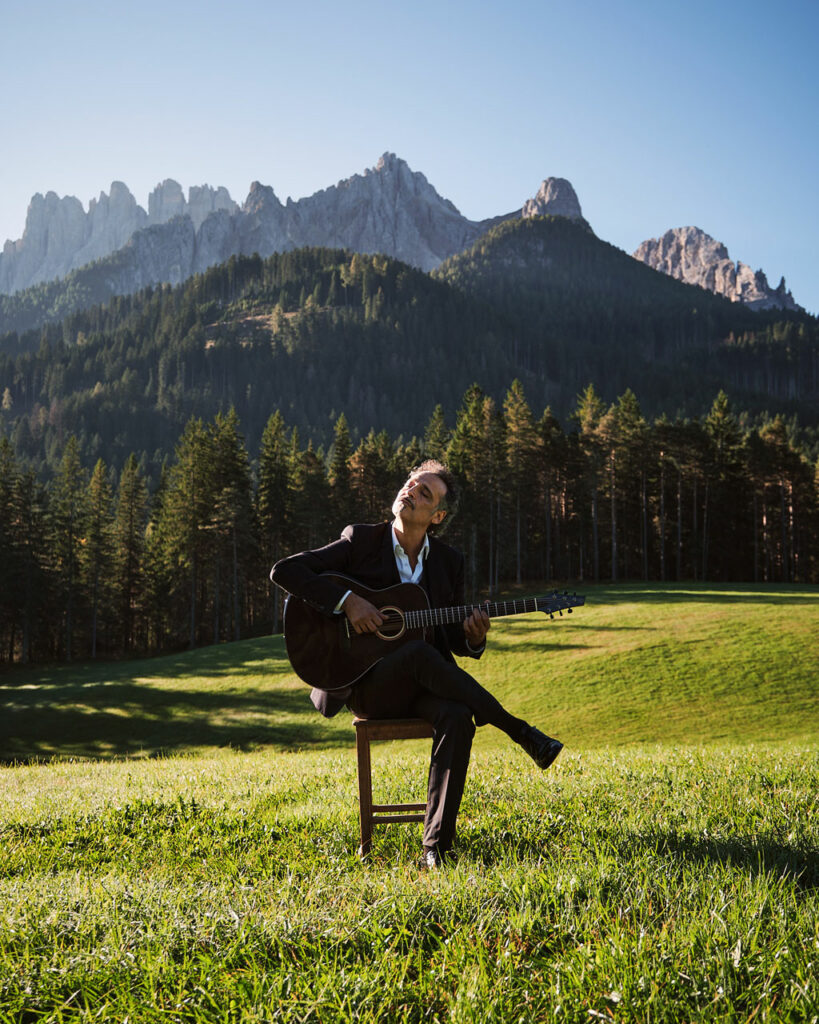 Guitarist playing a Thom Orgler Latemar acoustic (PU high-gloss Smokegrain) outdoors in the Dolomites, eyes closed, enjoying the performance.