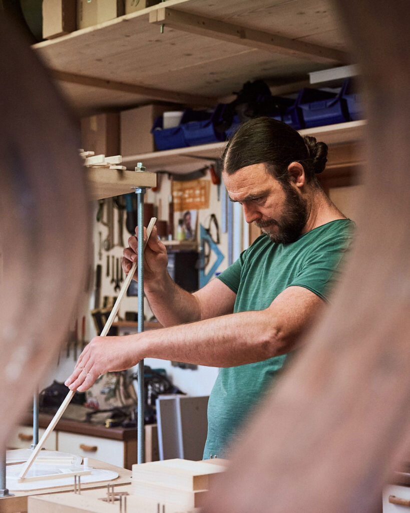 Thom Orgler, South Tyrolean luthier, shaping braces at his workshop bench while building a handcrafted acoustic guitar.