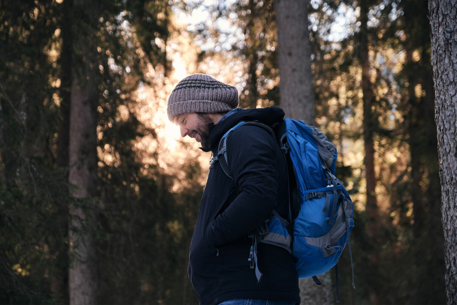 South Tyrolean luthier with a blue backpack smiling in a Dolomite winter forest at sunrise, scouting spruce for future tonewood.