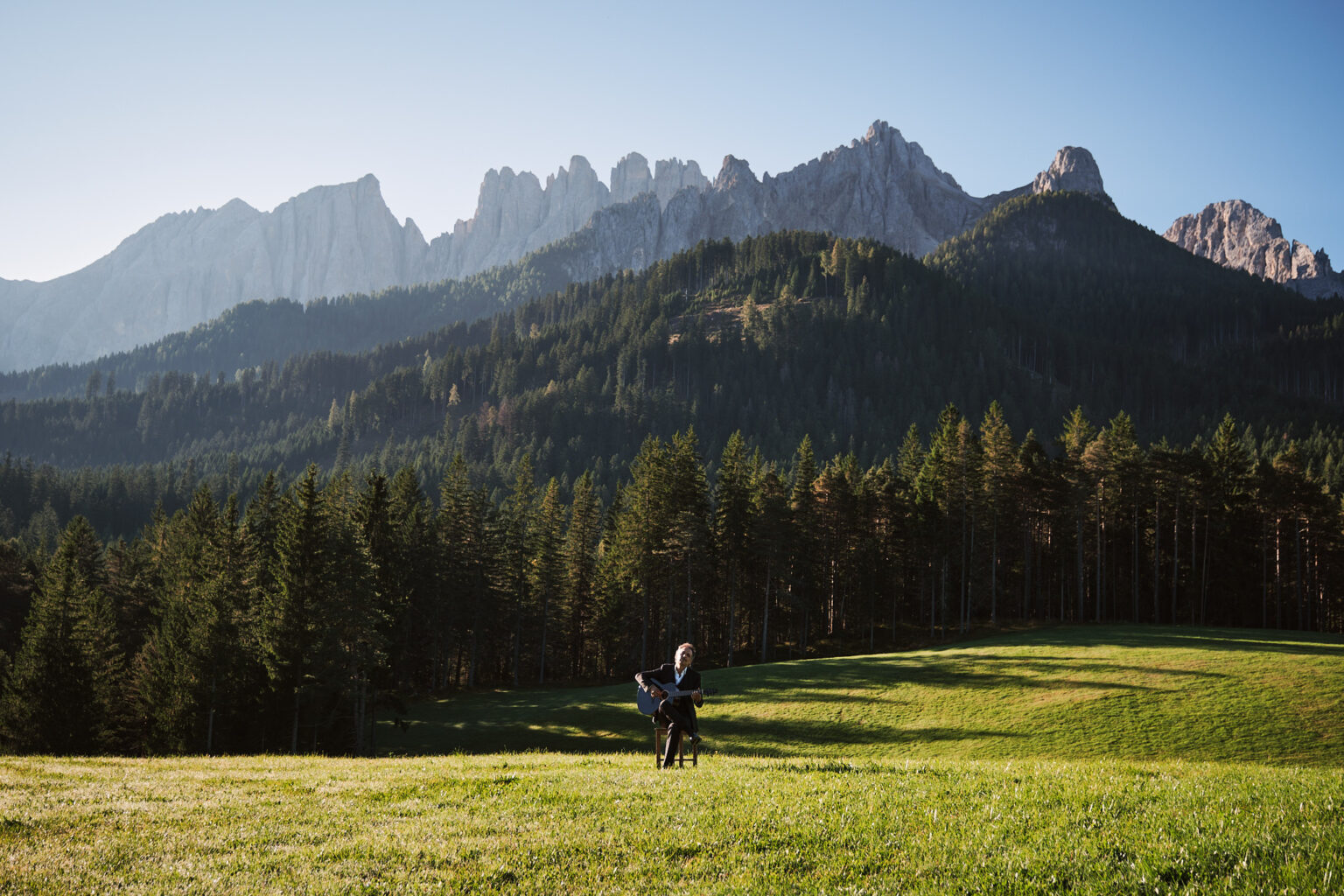 Guitarist playing a Thom Orgler Latemar acoustic (PU high-gloss Smokegrain) outdoors in the Dolomites, eyes closed, enjoying the performance.