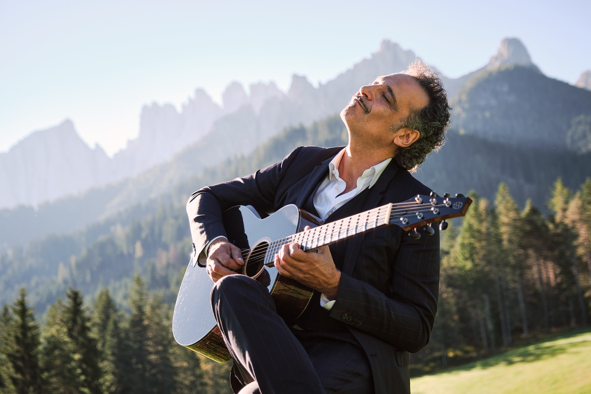 Guitarist playing a Thom Orgler Latemar acoustic (PU high-gloss Smokegrain) outdoors in the Dolomites, eyes closed, enjoying the performance.