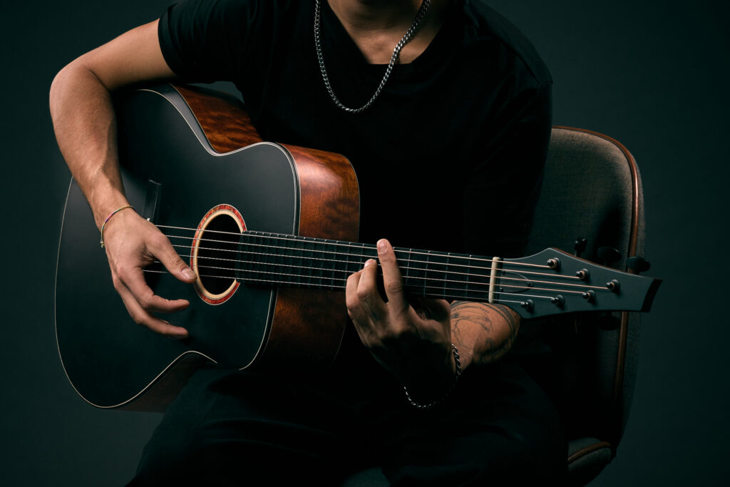 Guitarist playing a Thom Orgler Latemar baritone acoustic—dark top—studio close-up of hands, fretboard, and headstock.