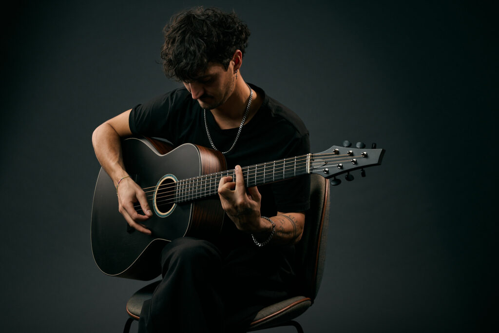 Guitarist playing a Thom Orgler Latemar baritone acoustic—dark top—studio close-up of hands, fretboard, and headstock.