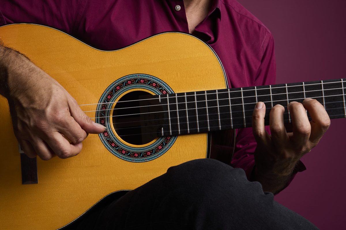 Close-up of a guitarist playing the Thom Orgler Enrosadira classical guitar, showing the decorative rosette, fretboard, and fingerpicking technique.