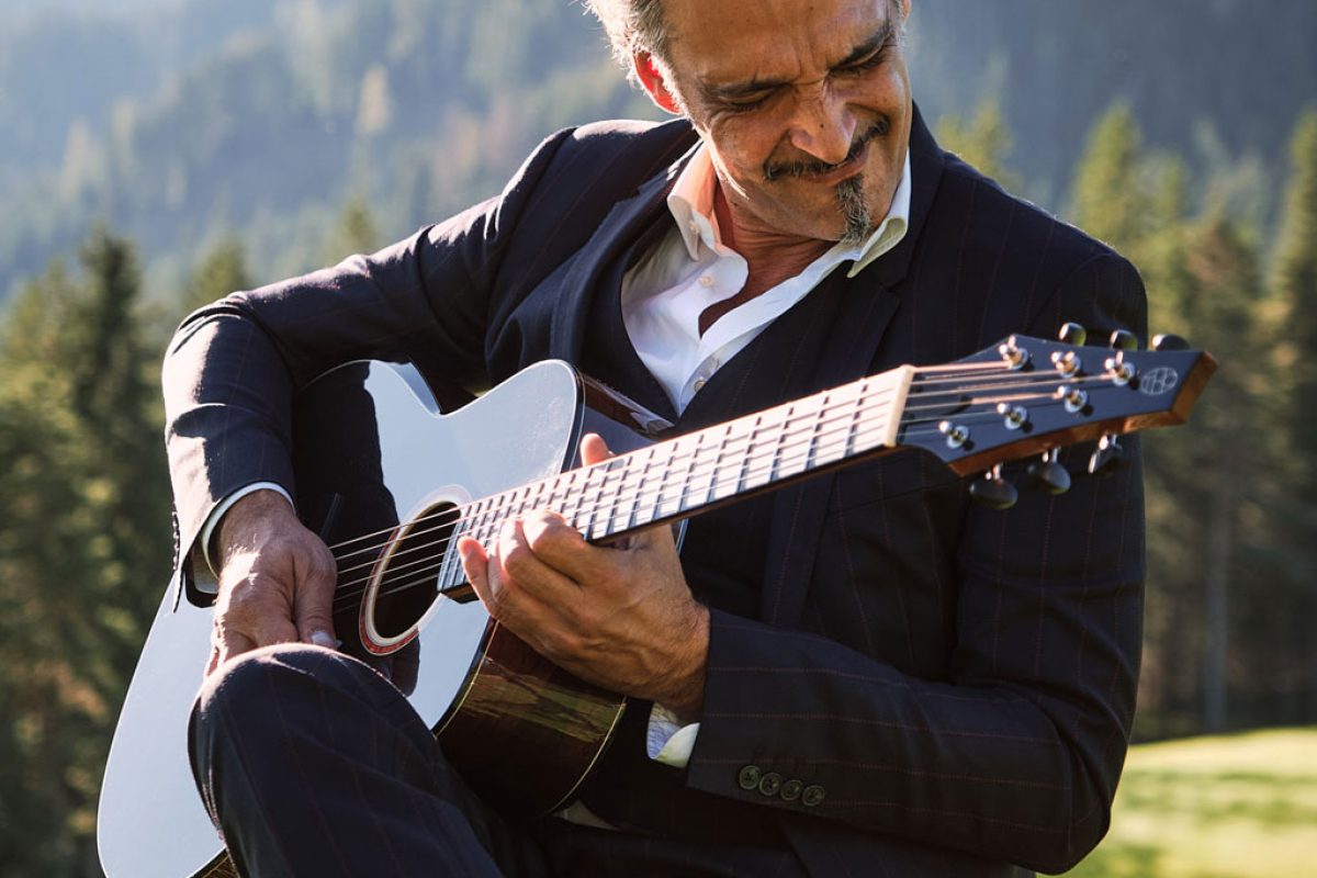 Guitarist playing a Thom Orgler Latemar acoustic (PU high-gloss Smokegrain) outdoors in the Dolomites, eyes closed, enjoying the performance.